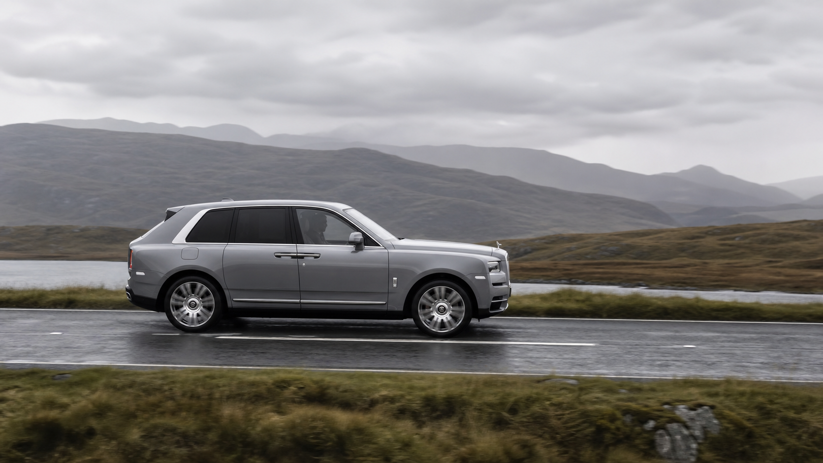 Rolls-Royce Cullinan gris roulant sur une route humide après la pluie