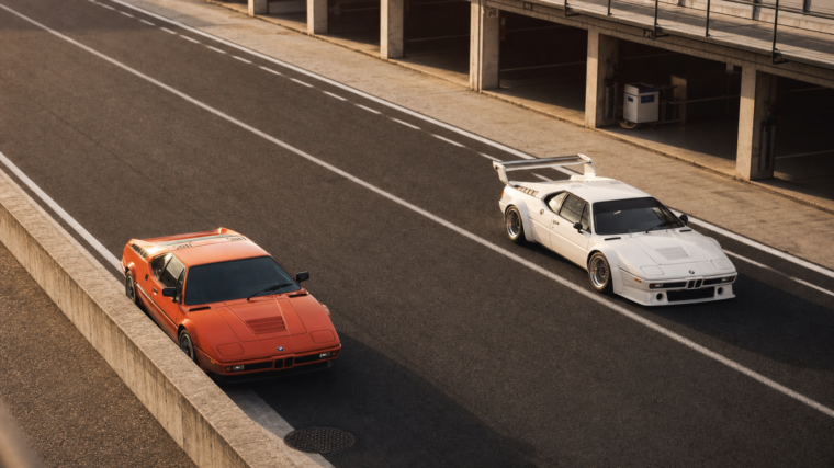 BMW M1 routière orange et BMW M1 Procar blanche dans les stands d’un circuit historique