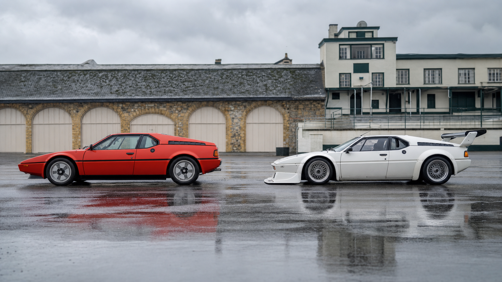BMW M1 routière rouge et voiture de compétition blanche observées de profil dans un paddock historique