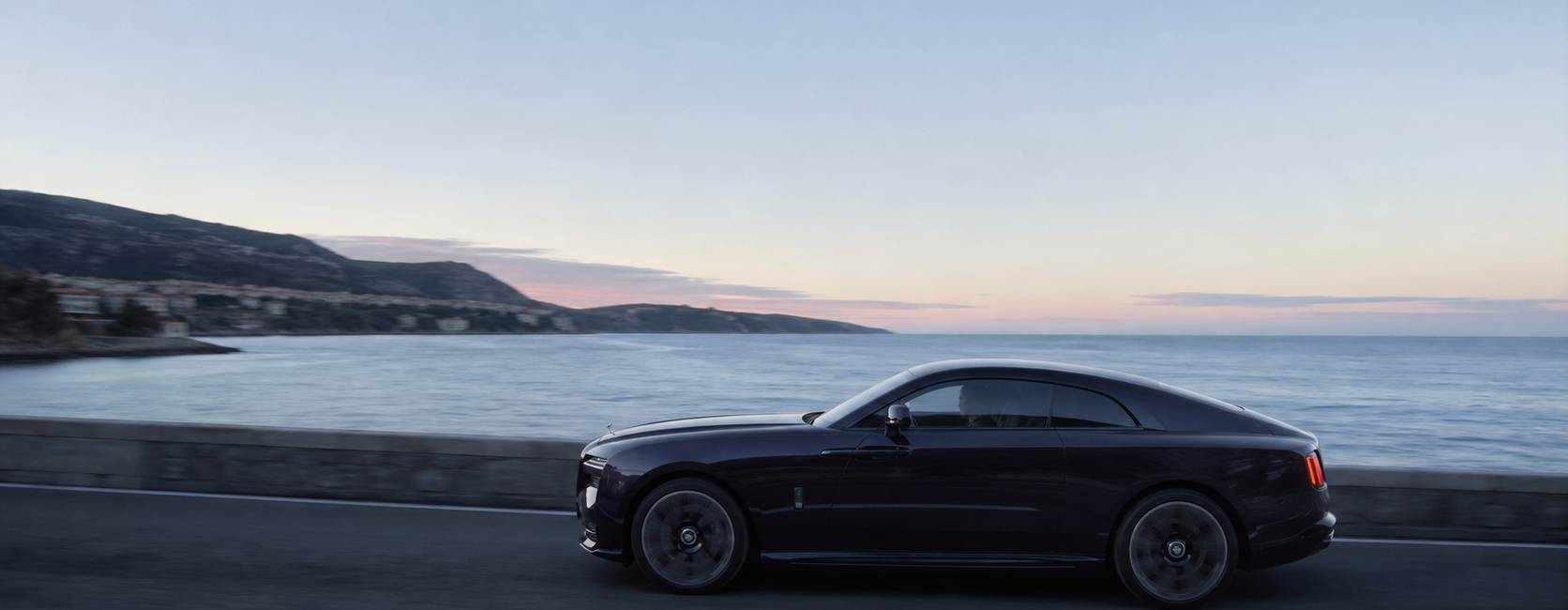 Grand coupé électrique de très grand luxe sombre roulant à l’aube sur une route côtière