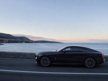 Grand coupé électrique de très grand luxe sombre roulant à l’aube sur une route côtière