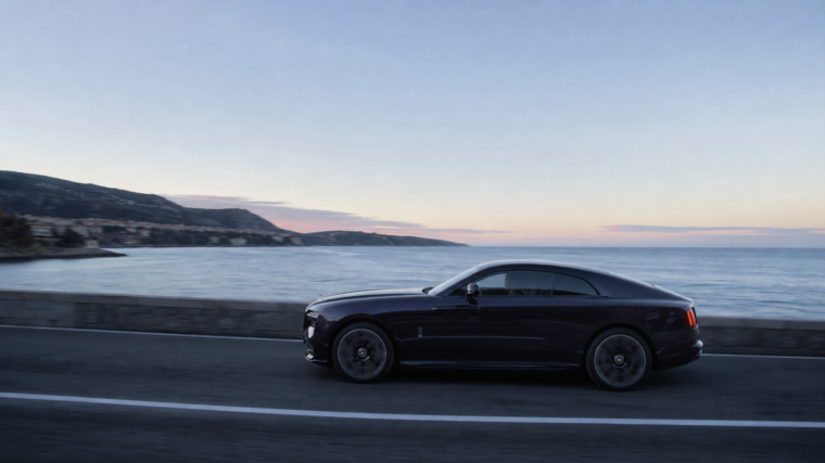 Grand coupé électrique de très grand luxe sombre roulant à l’aube sur une route côtière