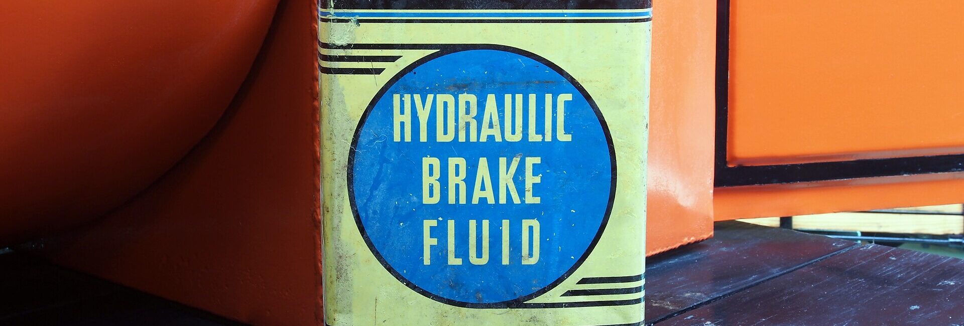 Ancien bidon Ford de liquide de frein hydraulique devant une voiture de collection orange