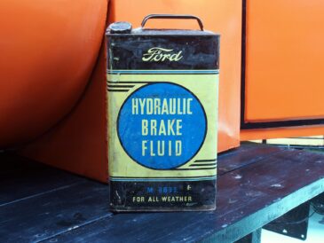 Ancien bidon Ford de liquide de frein hydraulique devant une voiture de collection orange
