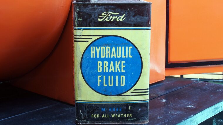 Ancien bidon Ford de liquide de frein hydraulique devant une voiture de collection orange