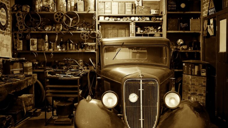 Voiture ancienne immobilisée dans un garage rempli de pièces et d’outils