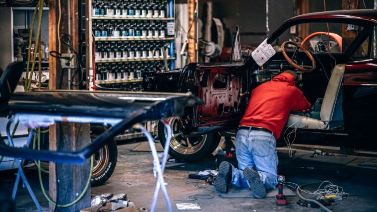 Technicien travaillant sur une voiture ancienne démontée dans un atelier de carrosserie
